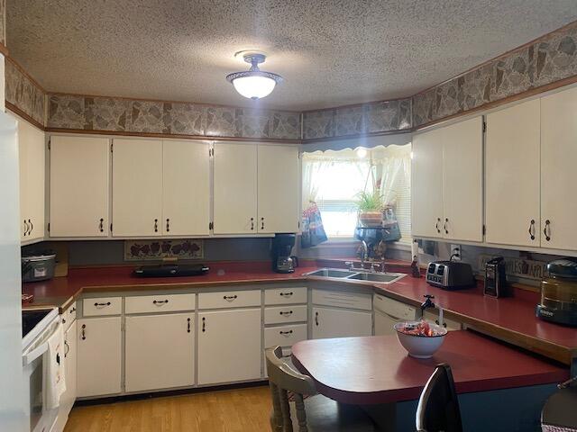 kitchen with white cabinetry, light hardwood / wood-style flooring, white stove, sink, and a textured ceiling