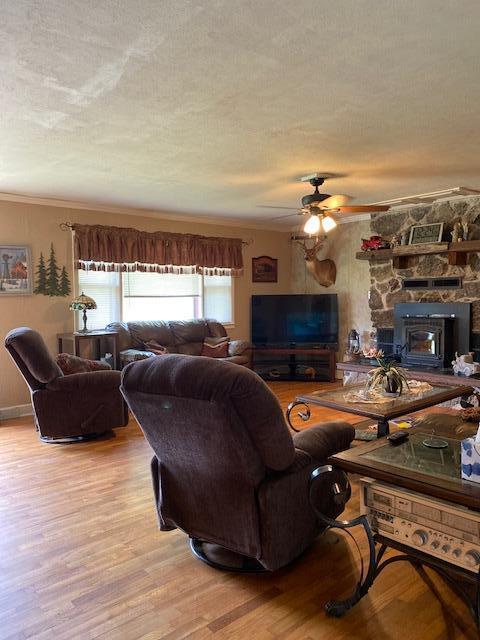 living room with ceiling fan, a wood stove, a textured ceiling, light wood-type flooring, and crown molding