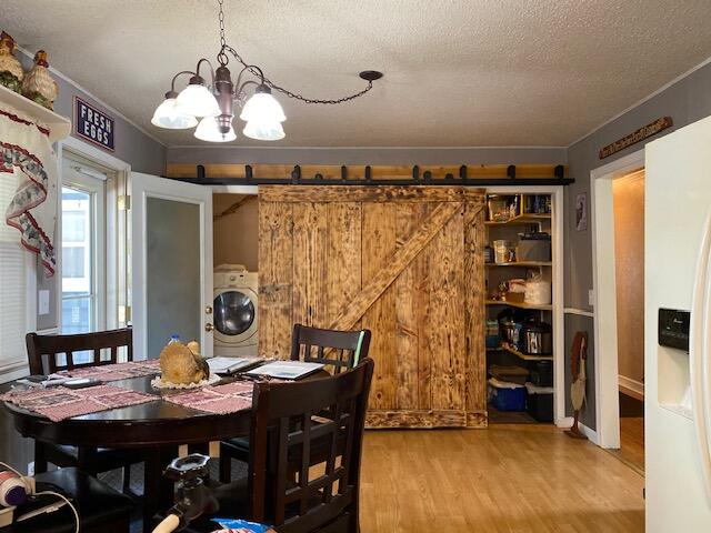 dining space featuring a barn door, a notable chandelier, washer / clothes dryer, hardwood / wood-style flooring, and a textured ceiling