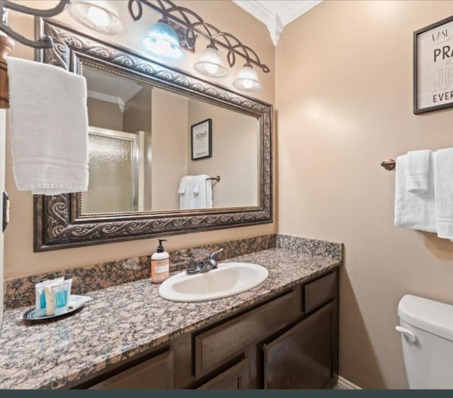 bathroom with vanity, crown molding, toilet, and a shower with shower door