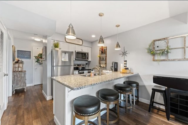 kitchen with dark wood-type flooring, decorative light fixtures, stainless steel appliances, kitchen peninsula, and white cabinetry