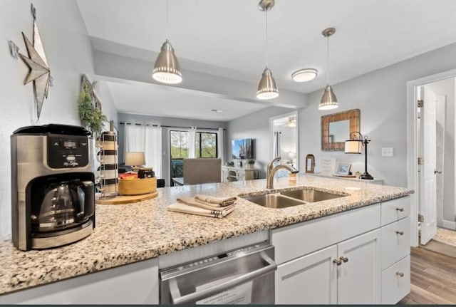 kitchen featuring light stone countertops, white cabinets, sink, pendant lighting, and light hardwood / wood-style flooring