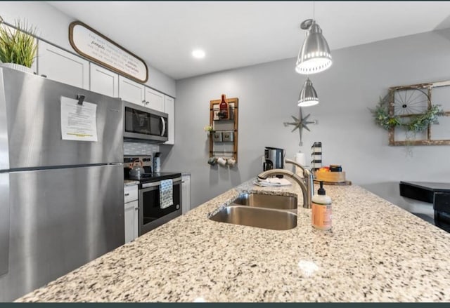 kitchen featuring light stone counters, a sink, decorative light fixtures, a center island with sink, and appliances with stainless steel finishes