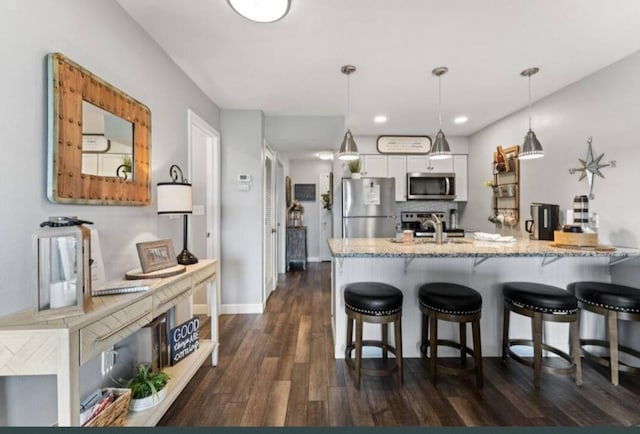 kitchen with dark hardwood / wood-style floors, kitchen peninsula, white cabinetry, appliances with stainless steel finishes, and decorative light fixtures