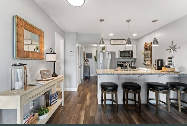 kitchen with a kitchen bar, pendant lighting, light stone countertops, dark wood-type flooring, and appliances with stainless steel finishes