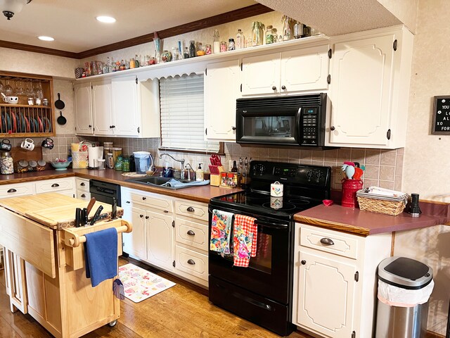 kitchen with light wood-type flooring, white cabinets, black appliances, backsplash, and sink