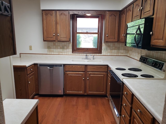 kitchen featuring dishwasher, backsplash, white electric range, sink, and hardwood / wood-style flooring