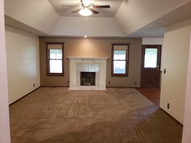 unfurnished living room with a healthy amount of sunlight, a raised ceiling, and a tiled fireplace