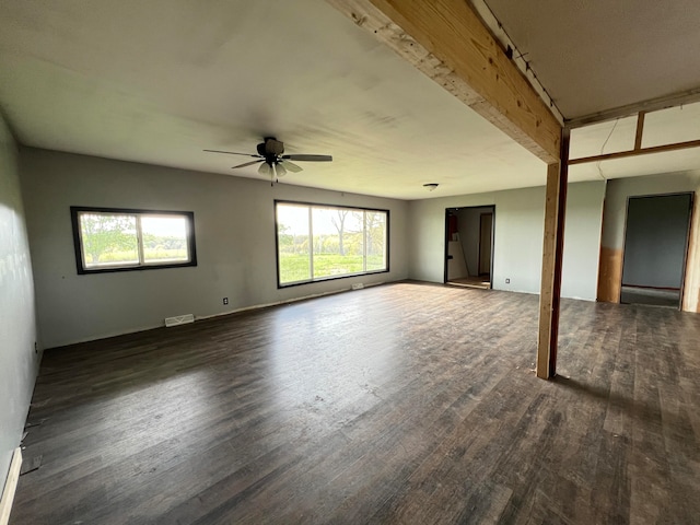 unfurnished living room featuring ceiling fan, a wealth of natural light, dark hardwood / wood-style floors, and beam ceiling