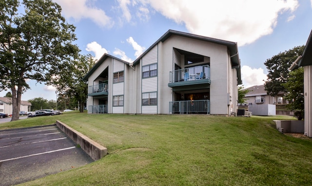 rear view of house with a balcony, a yard, and central air condition unit