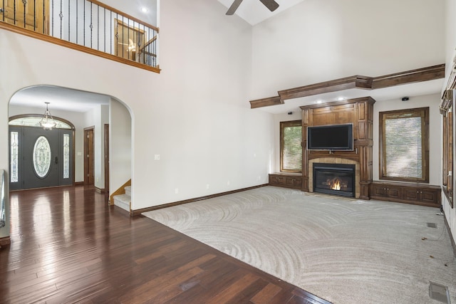 unfurnished living room with a towering ceiling, dark hardwood / wood-style floors, a large fireplace, and ceiling fan