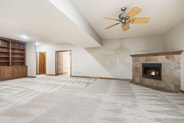 unfurnished living room with ceiling fan, light colored carpet, built in features, and a tile fireplace