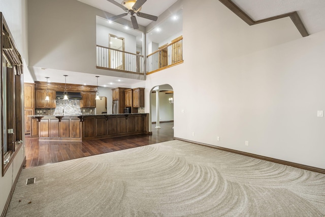 unfurnished living room featuring a towering ceiling, dark hardwood / wood-style floors, beam ceiling, and ceiling fan