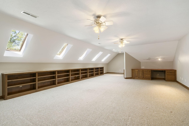additional living space with visible vents, a ceiling fan, baseboards, vaulted ceiling with skylight, and light colored carpet