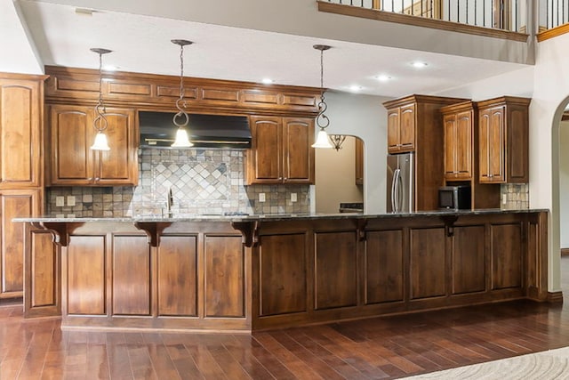kitchen featuring stainless steel appliances, arched walkways, dark stone countertops, decorative backsplash, and under cabinet range hood