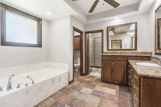 bathroom featuring ceiling fan, tiled tub, toilet, a raised ceiling, and vanity