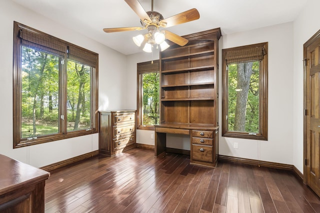 unfurnished office featuring a ceiling fan, baseboards, a healthy amount of sunlight, and dark wood-style floors