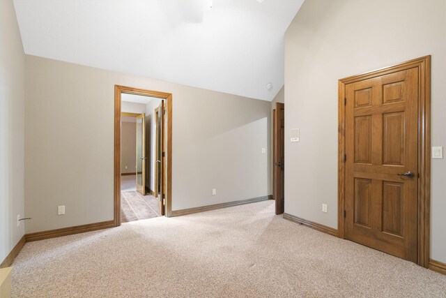 interior space featuring light carpet, lofted ceiling, and baseboards