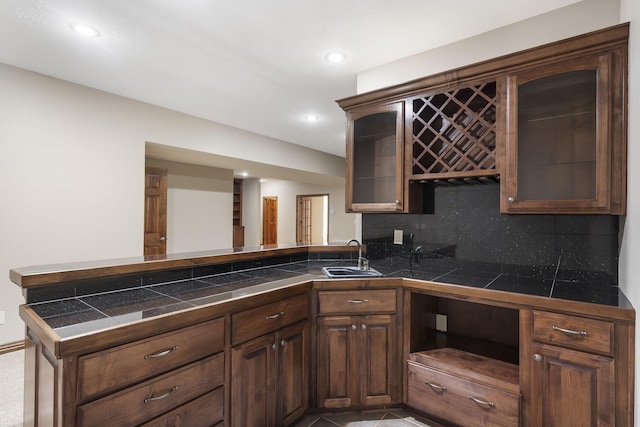 kitchen featuring kitchen peninsula, dark brown cabinetry, sink, and backsplash