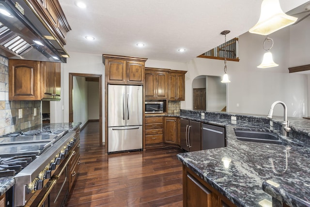 kitchen featuring stainless steel appliances, ventilation hood, a sink, arched walkways, and dark wood-style flooring