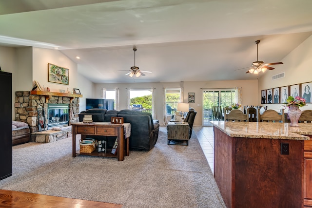 living room featuring light carpet, a stone fireplace, lofted ceiling, and ceiling fan