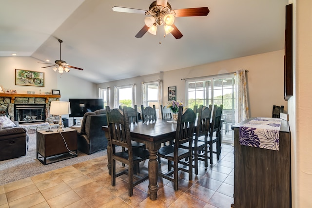 tiled dining area with ceiling fan, vaulted ceiling, and a stone fireplace