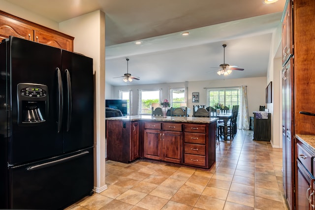 kitchen with light tile patterned floors, light stone countertops, black fridge with ice dispenser, and lofted ceiling