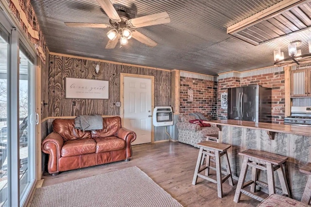 living room featuring wood-type flooring, heating unit, ceiling fan with notable chandelier, and wood walls