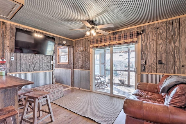 living room featuring light wood-type flooring, wooden walls, and ceiling fan