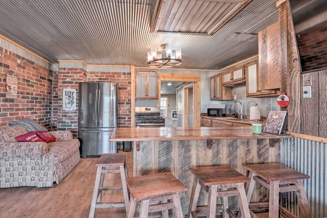 kitchen featuring sink, brick wall, appliances with stainless steel finishes, a breakfast bar, and light hardwood / wood-style floors