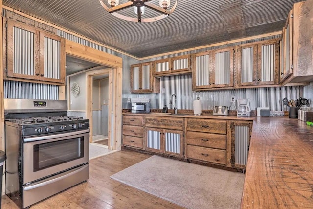 kitchen featuring stainless steel range with gas stovetop, crown molding, sink, and light wood-type flooring