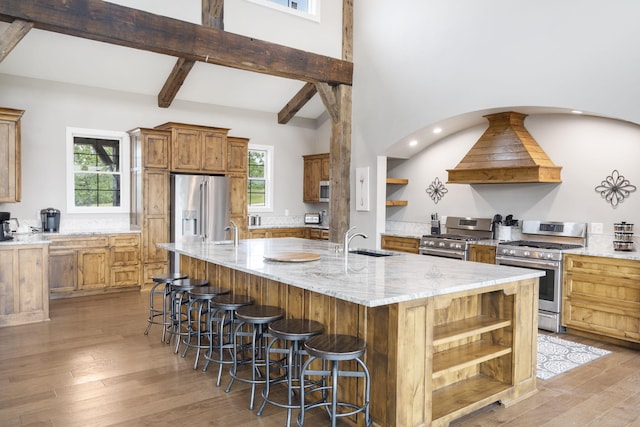 kitchen with light stone counters, a large island with sink, stainless steel appliances, a breakfast bar area, and light wood-type flooring