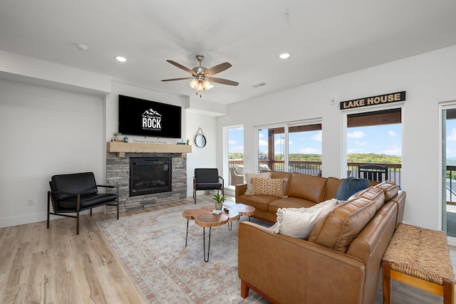 living room with ceiling fan, light wood-type flooring, and a stone fireplace