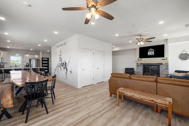 living room featuring a stone fireplace, light hardwood / wood-style flooring, and ceiling fan