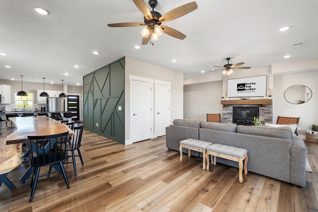 living room with ceiling fan, a fireplace, and light hardwood / wood-style floors