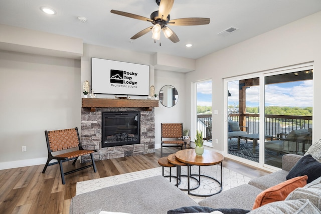 living room featuring wood-type flooring, ceiling fan, and a stone fireplace