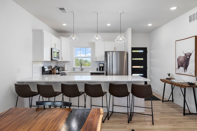 kitchen with white cabinets, hanging light fixtures, sink, stainless steel appliances, and light hardwood / wood-style floors