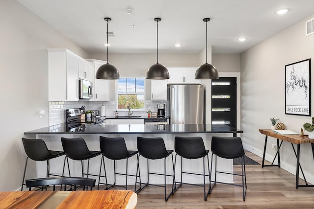 kitchen with white cabinets, sink, light hardwood / wood-style floors, hanging light fixtures, and appliances with stainless steel finishes