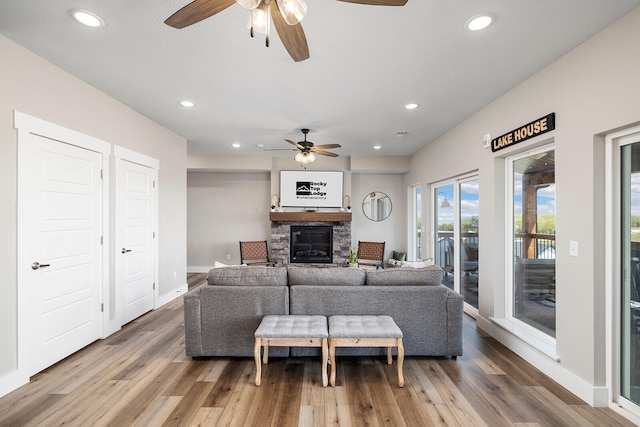 living room with ceiling fan, a stone fireplace, and wood-type flooring