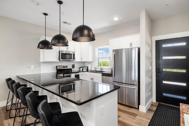 kitchen featuring pendant lighting, sink, kitchen peninsula, appliances with stainless steel finishes, and white cabinetry