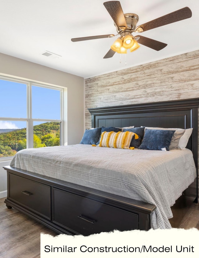bedroom featuring wood walls, wood finished floors, visible vents, an accent wall, and ceiling fan