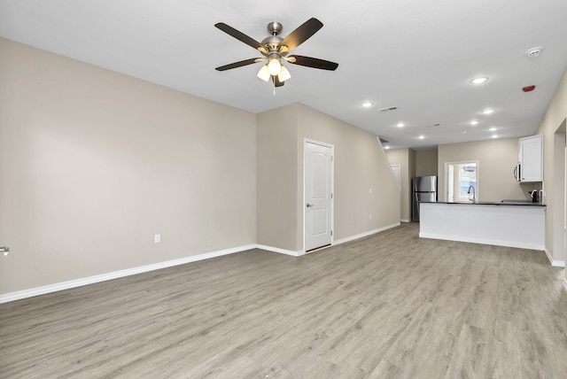 unfurnished living room featuring light wood-style flooring, baseboards, ceiling fan, and a sink