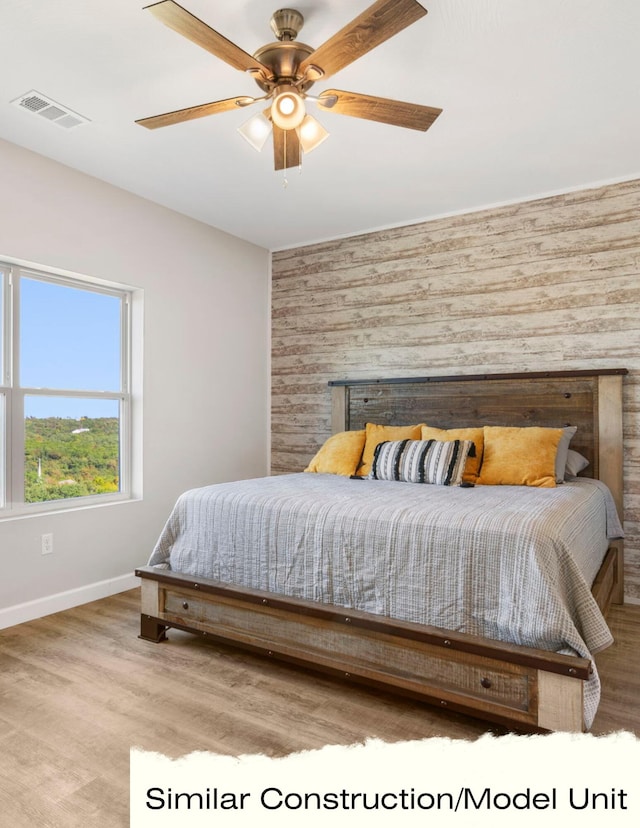 bedroom featuring wood finished floors, wooden walls, ceiling fan, baseboards, and visible vents