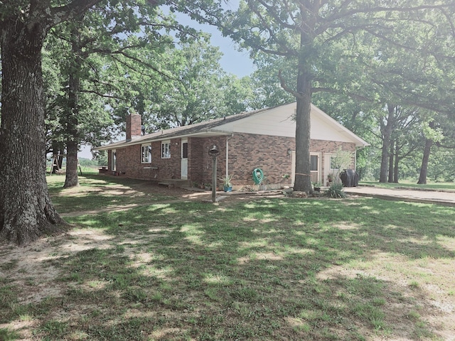 view of side of home featuring a lawn, a chimney, and brick siding