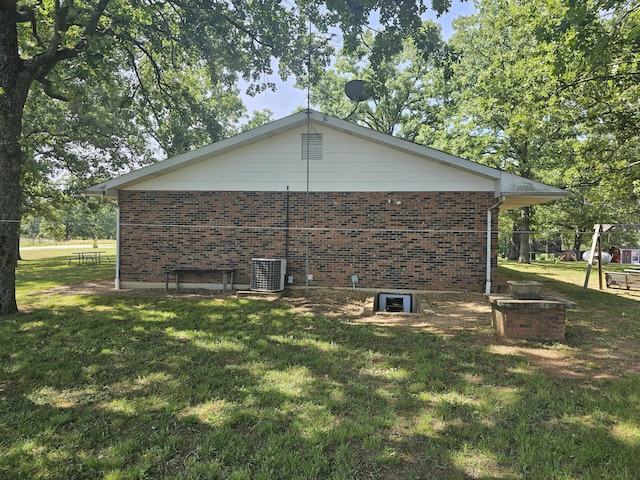 view of side of home with a lawn, brick siding, and central AC