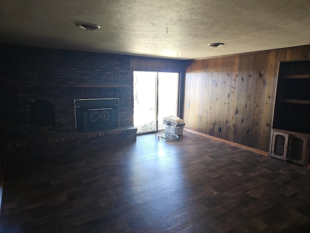 unfurnished living room featuring wooden walls, wood finished floors, baseboards, a fireplace, and a textured ceiling
