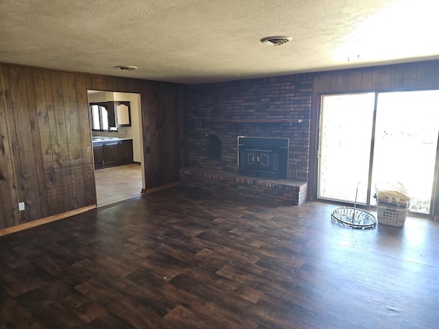 unfurnished living room with wooden walls, a fireplace, wood finished floors, and a textured ceiling