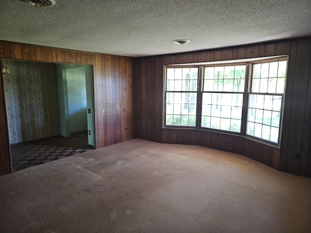 empty room featuring visible vents, wood walls, and a textured ceiling