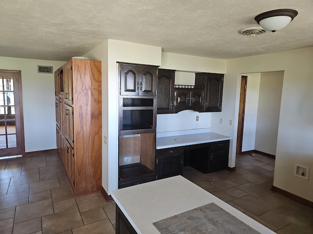kitchen with light countertops, a textured ceiling, visible vents, and baseboards