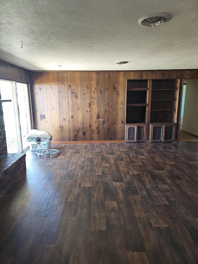 empty room featuring wood finished floors, a textured ceiling, and wood walls